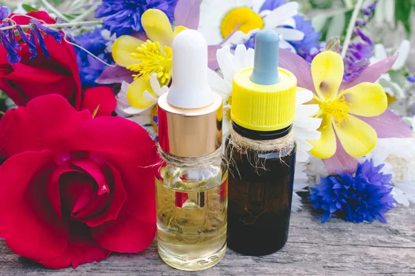 Aceite esencial con una rosa en una botella de vidrio cerca de flores silvestres sobre fondo de madera . —  Fotos de Stock