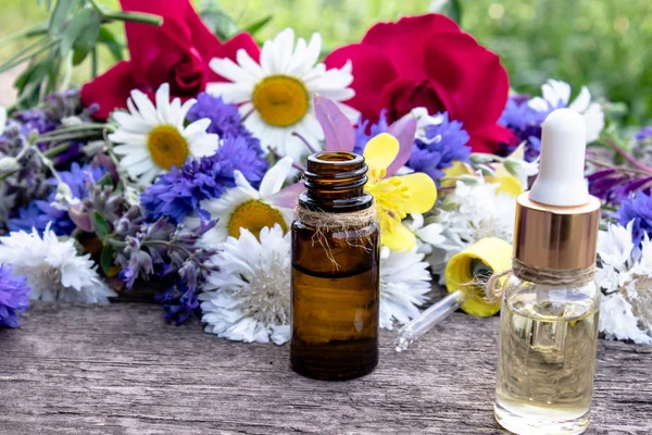 Aceite esencial en una botella de vidrio cerca de flores silvestres sobre fondo de madera . — Foto de Stock