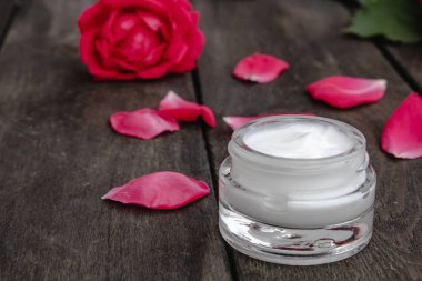 Ahşap rustik arka plan üzerinde bir cam kavanozda yüz ve vücut bakımı için kırmızı pembe çiçekler ile Doğal çiçek kozmetik