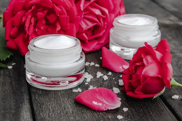 Natural flower cosmetics with red pink flowers for face and body care in a glass jar on a wooden rustic background