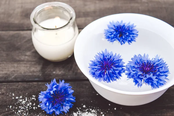 Kék cornflowers hazugság a vízben egy fehér tál közelében égő gyertyát a háttérben a régi táblák. — Stock Fotó