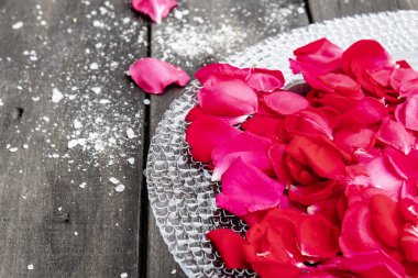 Gül yaprakları eski koyu ahşap tahtalar üzerinde bir tabak üzerinde yalan.