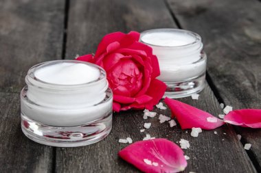 Ahşap rustik arka plan üzerinde bir cam kavanozda yüz ve vücut bakımı için kırmızı pembe çiçekler ile Doğal çiçek kozmetik