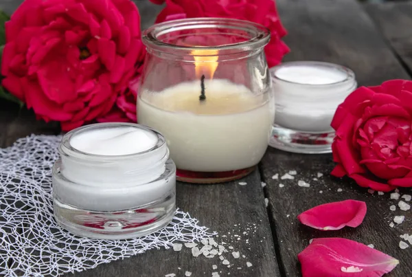 Crema cosmetica e rose con petali e una candela accesa sul vecchio sfondo di legno . — Foto Stock