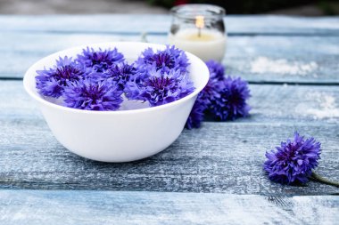 mavi cornflowers mavi eski kurulların arka plan karşı yanan bir mum yanında beyaz bir kapta suda yalan.