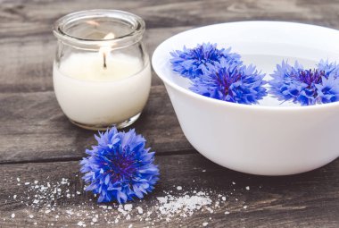 mavi cornflowers eski kurulların arka planda yanan bir mum yakınında beyaz bir kapta suda yalan.