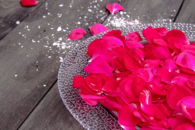 Gül yaprakları eski koyu ahşap tahtalar üzerinde bir tabak üzerinde yalan.