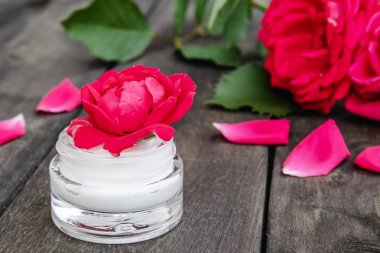 Ahşap rustik arka plan üzerinde bir cam kavanozda yüz ve vücut bakımı için kırmızı pembe çiçekler ile Doğal çiçek kozmetik