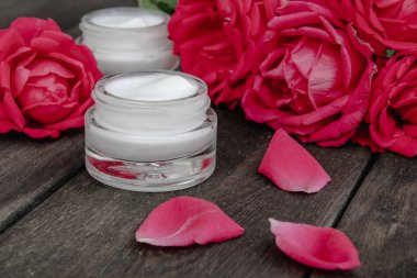 Ahşap rustik arka plan üzerinde bir cam kavanozda yüz ve vücut bakımı için kırmızı pembe çiçekler ile Doğal çiçek kozmetik