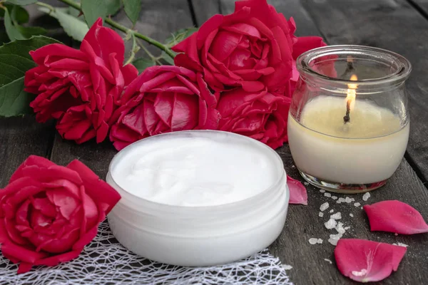 Cosmetic cream and roses with petals and a burning candle on the old wooden background. — Stock Photo, Image