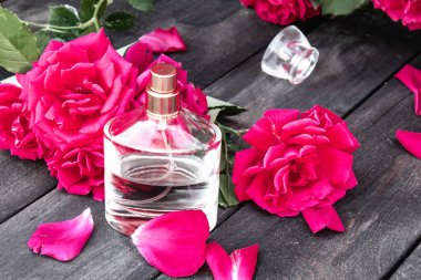 Koyu ahşap panoları bir arka plan üzerinde gül çiçekleri ile parfüm Şişesi.