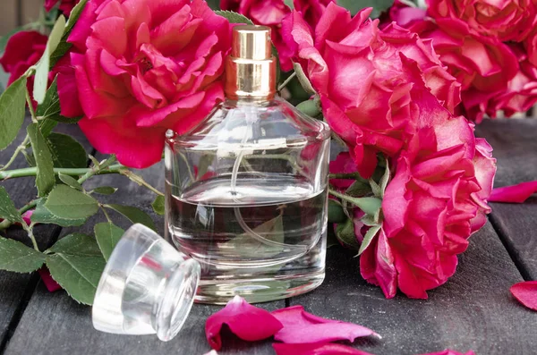 Garrafa de perfume com flores de rosas em um fundo de placas de madeira escuras . — Fotografia de Stock