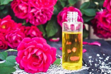 Ahşap bir masa üzerinde kırmızı gül ile kokulu yağ şişesi.
