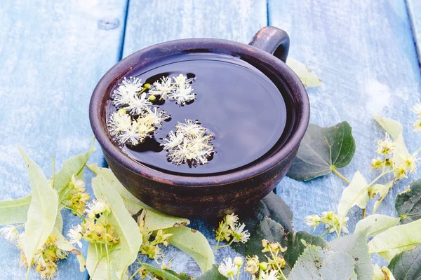 Чашка липового чая рядом с цветами лайма на фоне старых синих досок. цветы липы и чашку чая . — стоковое фото