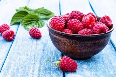 Mavi panoları arka plan karşı bir kase üzerinde olgun kırmızı ahududu. Seçici odaklama.