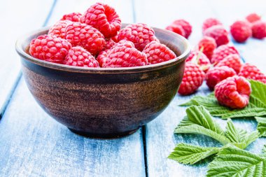 Mavi panoları arka plan karşı bir kase üzerinde olgun kırmızı ahududu. Seçici odaklama.