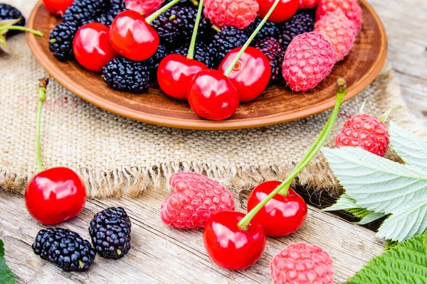 Frutti di bosco misti lamponi, ciliegie, gelsi in una ciotola su tela e fondo di legno . — Foto Stock