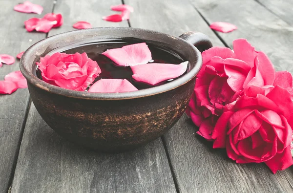 Tea from tea rose petals in a cup on a wooden rustic background.