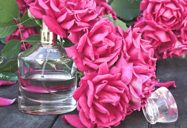 Butelka perfum otoczona czerwonymi różami. — Zdjęcie stockowe