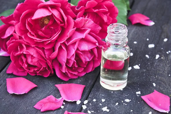 Aceite esencial con pétalos de rosa roja sobre fondo de madera oscura . — Foto de Stock