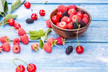 Meyve ve çilek mavi ahşap arka plan üzerinde bir kase içinde. Olgun ahududu, kiraz, dut.