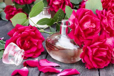Parfüm şişesi kırmızı güllerle çevrili.