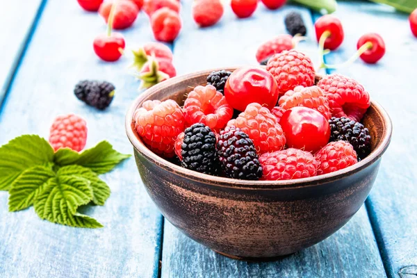 水果和浆果在蓝色木制背景的碗中。成熟的树莓，樱桃，桑树. — 图库照片