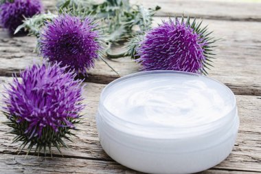 Ahşap arka plan üzerinde kozmetik yüz kremi açık kavanoz ile Thistle çiçek. Tıbbi bitki.