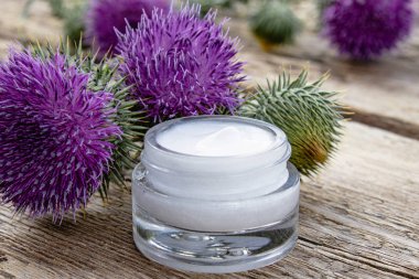 Ahşap arka plan üzerinde kozmetik yüz kremi açık kavanoz ile Thistle çiçek. Tıbbi bitki.
