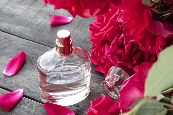 Botella de perfume de mujer con rosas rojas en el fondo de tablas de madera oscura . — Foto de Stock