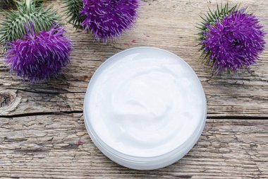 Ahşap arka plan üzerinde kozmetik yüz kremi açık kavanoz ile Thistle çiçek. Tıbbi bitki.
