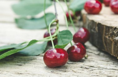 Ahşap masada yeşil yaprakları ile kırmızı kiraz ve dalları.