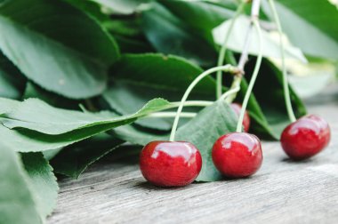 Ahşap masada yeşil yaprakları ile kırmızı kiraz ve dalları.