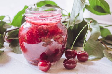 Ahşap tahta bir masada yeşil yaprakları bir arka planda bir cam kavanoz kiraz reçel.