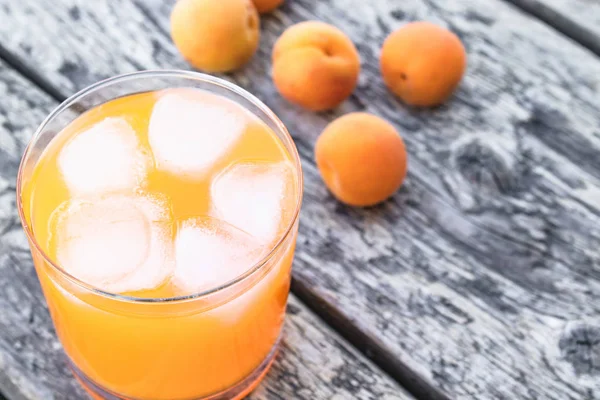 Succo di albicocca fresco con albicocche e cubetti di ghiaccio in un bicchiere sullo sfondo di vecchie tavole. Bevande alcoliche estive . — Foto Stock