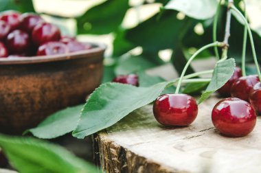 Ahşap masada yeşil yaprakları ile kırmızı kiraz ve dalları.