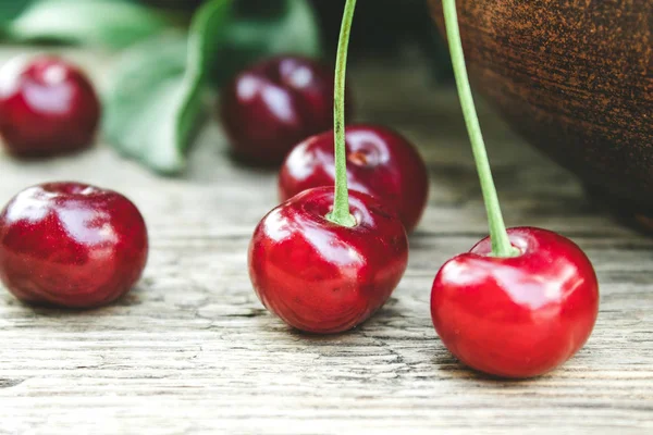 Red cherries and branches with green leaves on a wooden table. — Stock Photo, Image