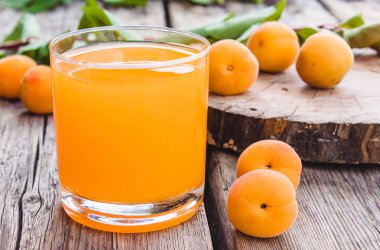 Kayısı ve eski tahtaları arka planda yeşil yaprakları ile bir şube ile taze kayısı suyu.