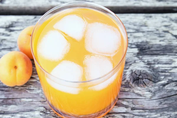 Suco de damasco fresco com damascos e cubos de gelo em um copo contra o fundo de tábuas antigas. Refrigerantes de verão . — Fotografia de Stock