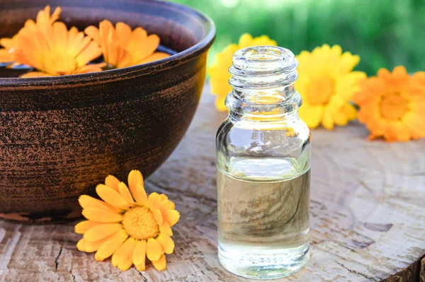 Aromatherapy essential oil with calendula flowers on a wooden background in nature. Extract of calendula tincture in a bowl. — Stock Photo, Image