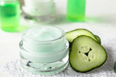 Beyaz ahşap arka planda taze salatalık dilimleri yanında salatalık özü ile bir cam kavanoz yüz kremi.