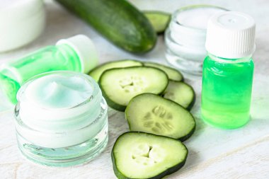 Beyaz ahşap arka planda taze salatalık dilimleri yanında salatalık özü ile bir cam kavanoz yüz kremi.