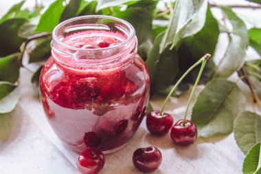 Ahşap tahta bir masada yeşil yaprakları bir arka planda bir cam kavanoz kiraz reçel.