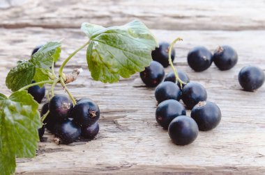 Siyah frenk üzümü ahşap arka planda yeşil yaprakları yanında yatıyor. Sulu doğal meyveler frenk üzümü.