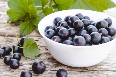 Yeşil yaprakları yakın ahşap arka planda beyaz bir kase taze olgun frenk üzümü çilek. Sulu meyve frenk üzümü. Siyah frenk üzümü