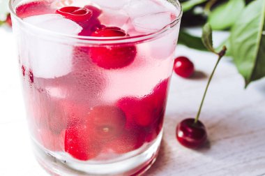 Beyaz ahşap arka planda kiraz ve buz ile kırmızı kokteyl. Kiraz ve buz küpleri ile taze yaz kokteyli.