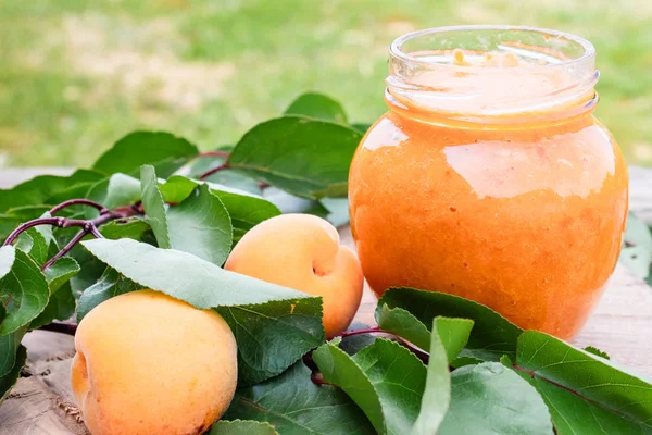 Cam bir kavanozda kayısı reçeli ve ahşap bir masada olgun kayısı.