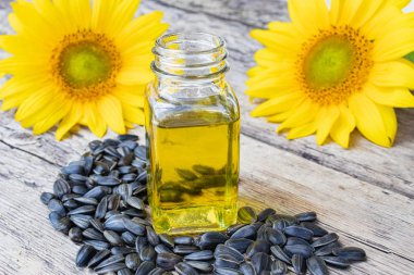Ayçiçeği çiçekleri yakınında ahşap bir arka plan üzerinde cam bir kavanoz ve ayçiçeği tohumu ayçiçek yağı.