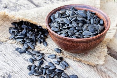 Tahta bir arka plan üzerinde bir kase ayçiçeği tohumu yığını. Masaya serpişne ayçiçeği tohumu.