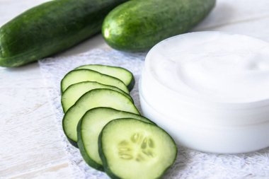 Beyaz ahşap arka planda taze salatalık dilimleri ile beyaz bir kavanoz yüz kremi.